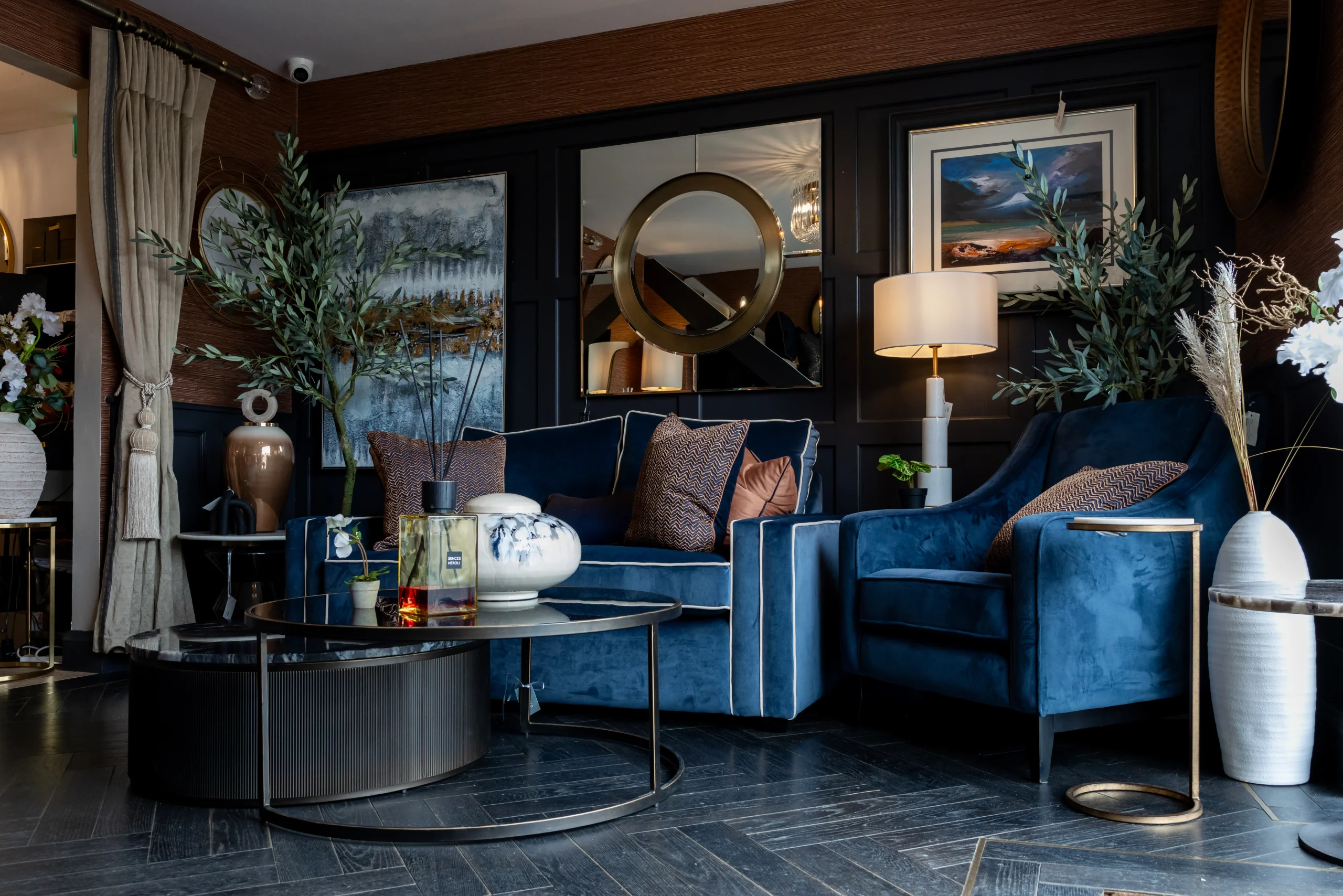 Navy velvet sofa and armchair with rust cushions, dark round coffee table and gold circle mirror at Gavelle Interiors Dublin