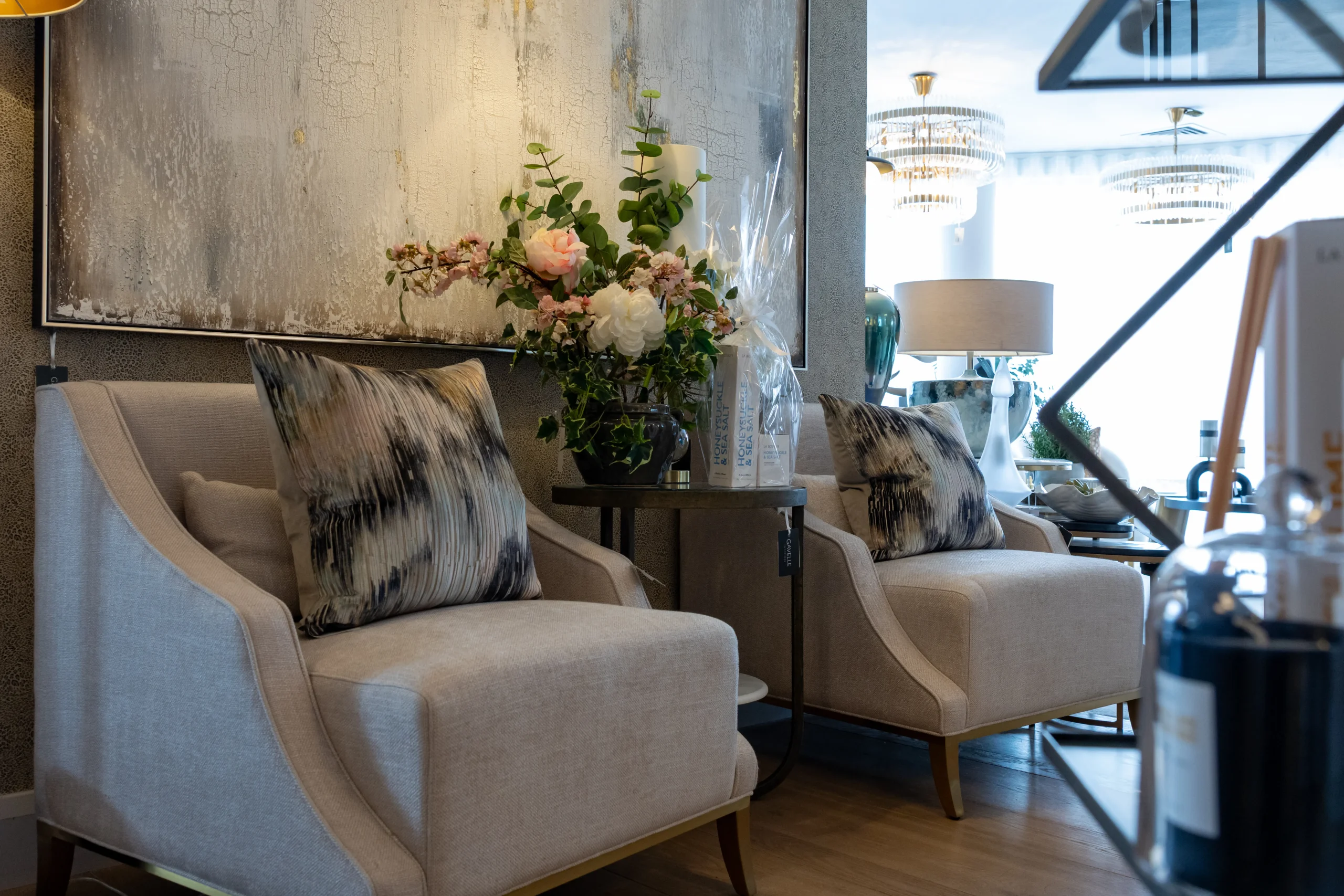 Pair of cream linen armchairs with navy ikat cushions beside abstract silver gold wall art