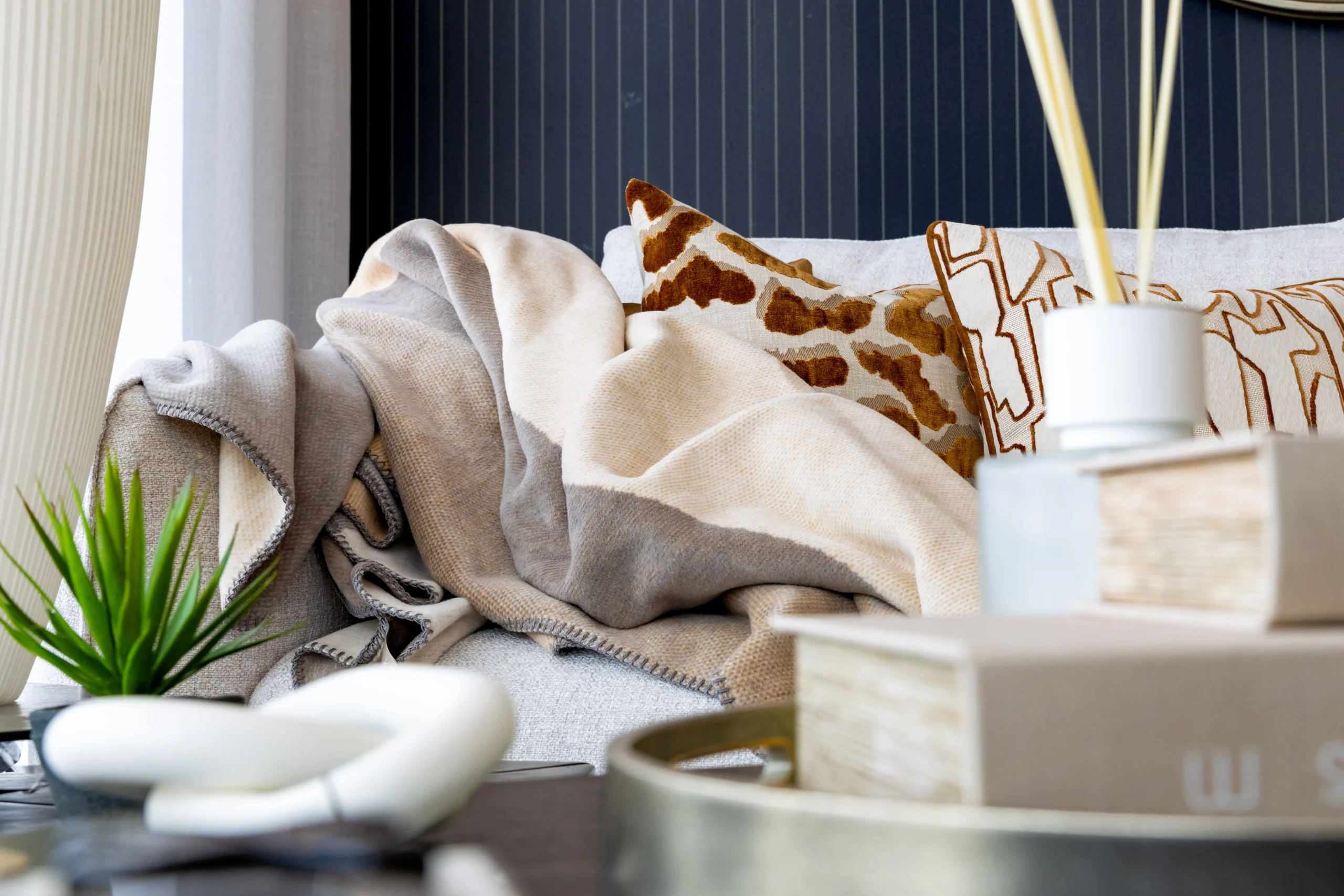 Beige wool throw with giraffe print velvet cushion and white reed diffuser on grey sofa