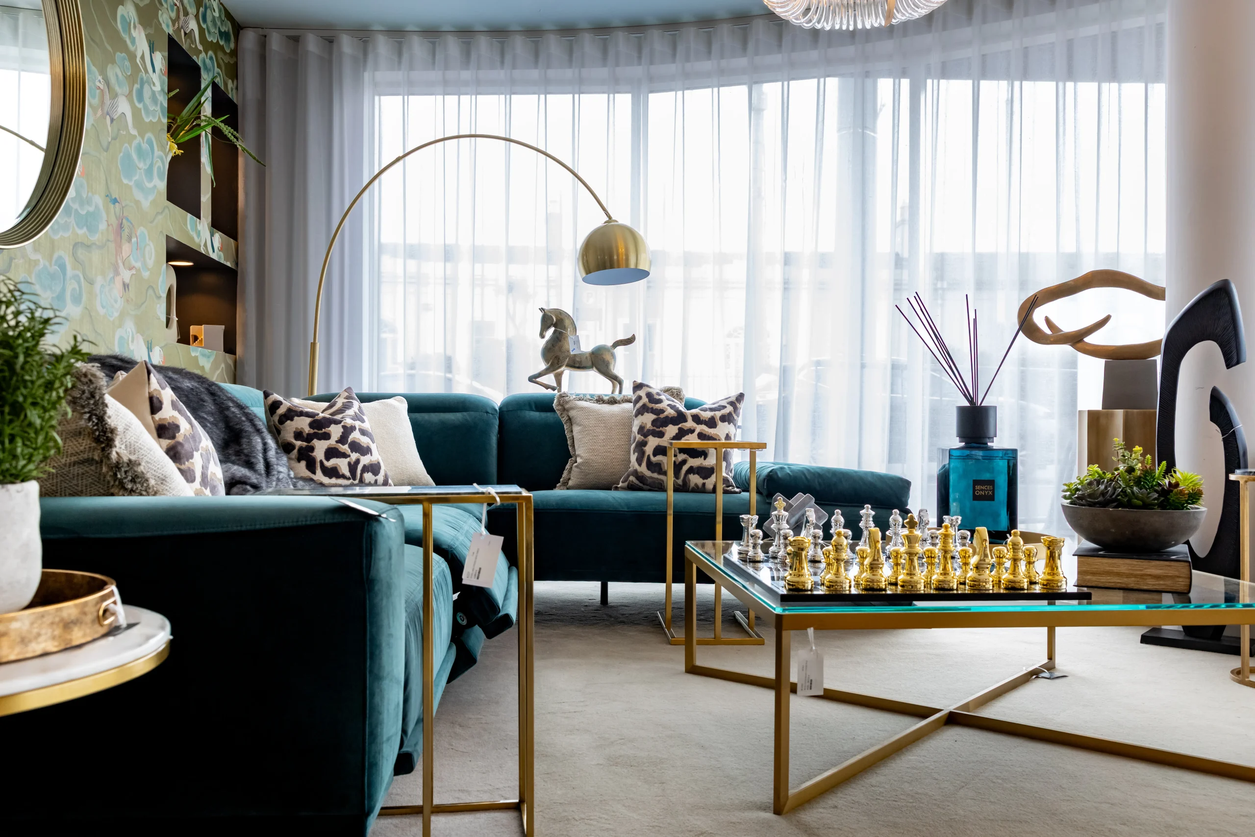 Teal velvet sofa with leopard print cushions, gold arc floor lamp and glass coffee table