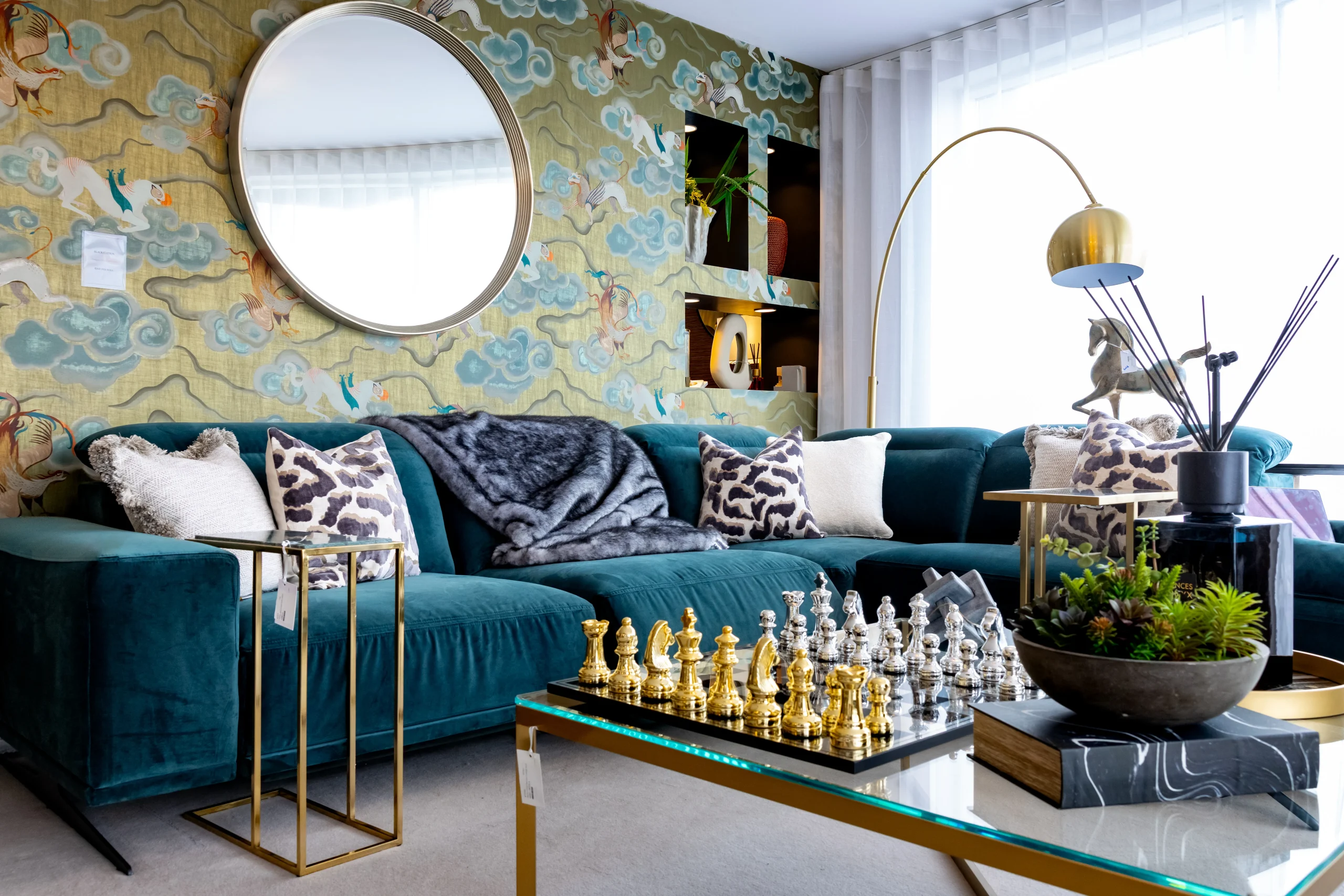 Soft, sculptural teal velvet corner sofa with brass arc floor lamp and glass coffee table