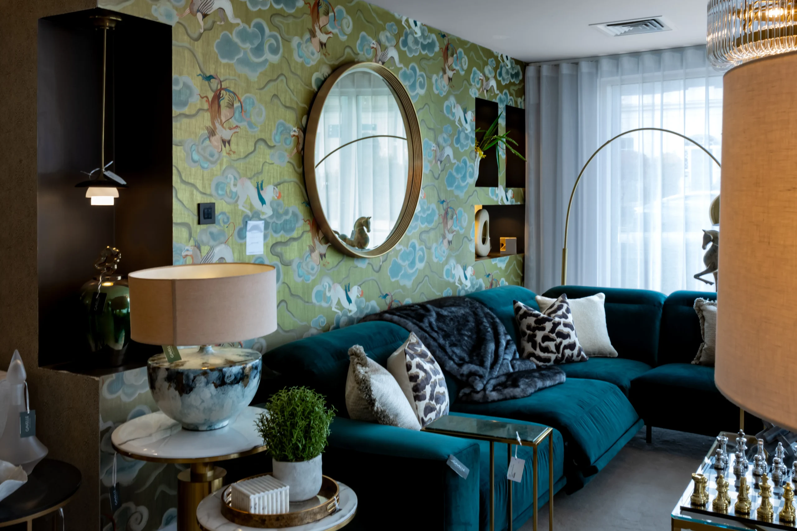 Teal velvet sectional sofa with faux fur throw and round gold mirror on chinoiserie wallpaper