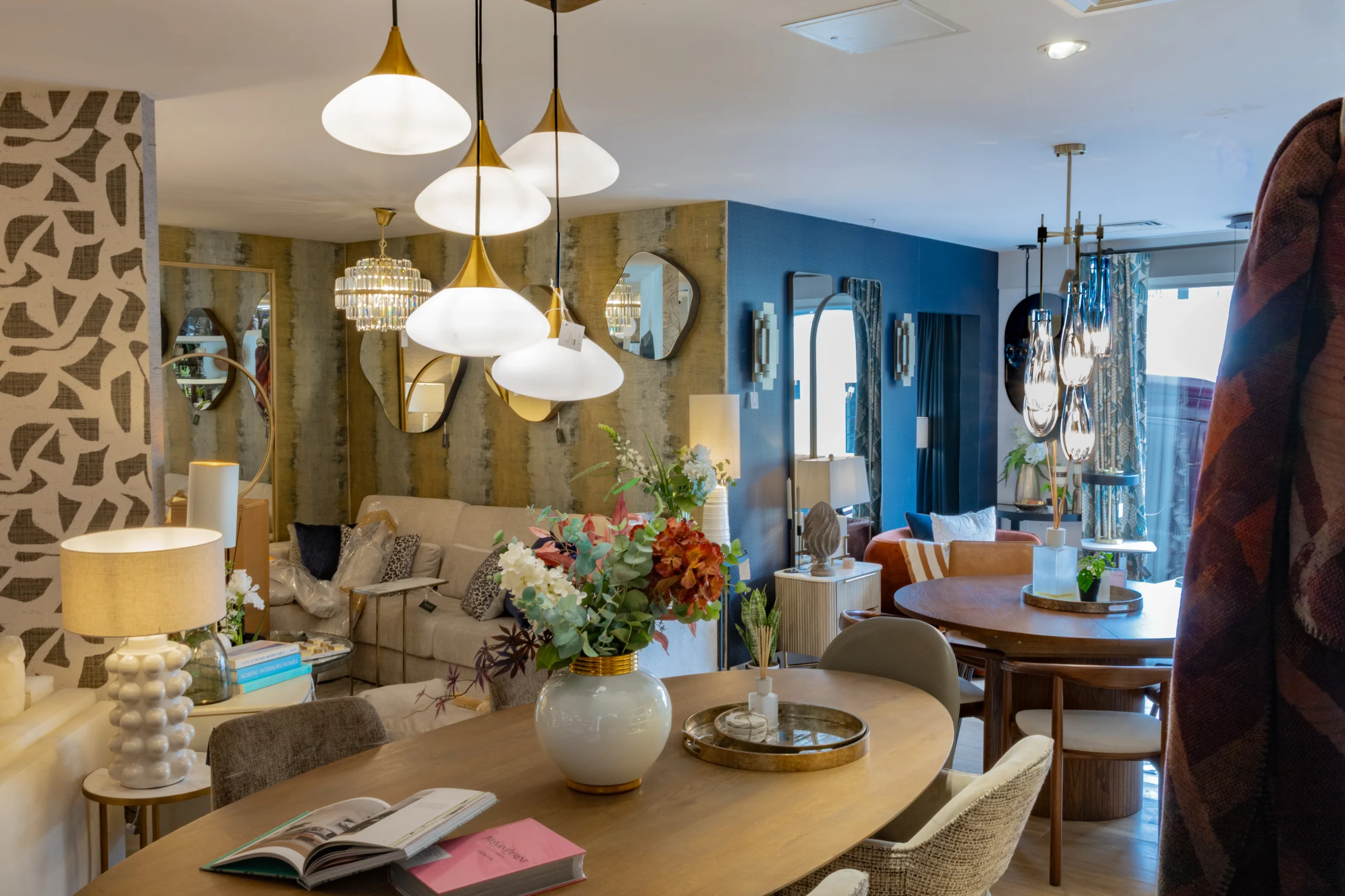 Gavelle interiors showroom with gold pendant lights, oval dining table and teal armchairs