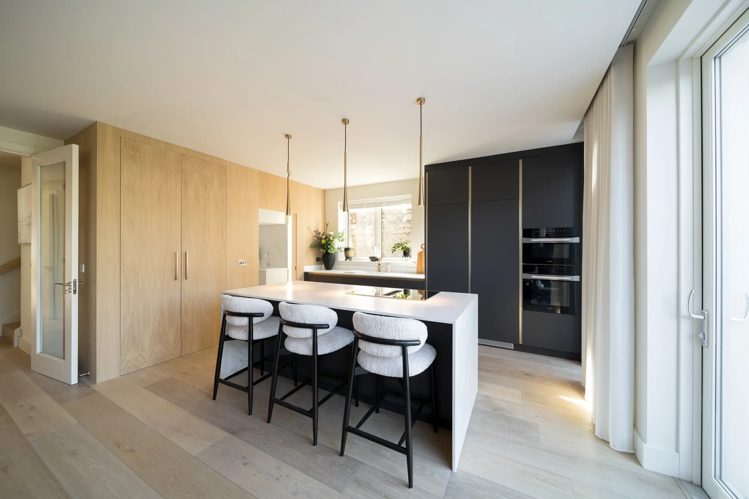 Wide view of the kitchen island, warm oak joinery and full-height glazing to the garden
