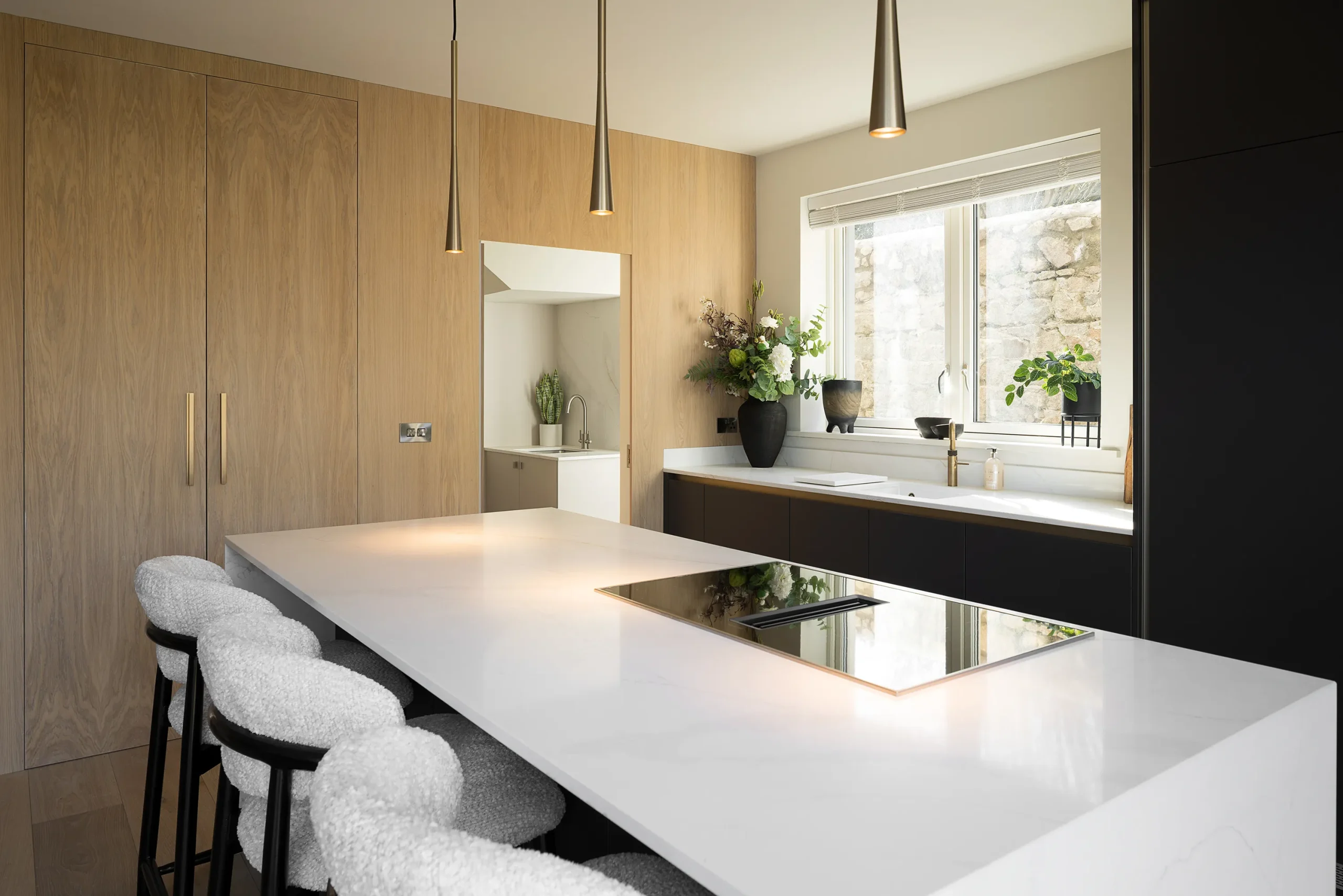 Quartz island detail with integrated downdraft hob, brass pendants and oak panelled wall