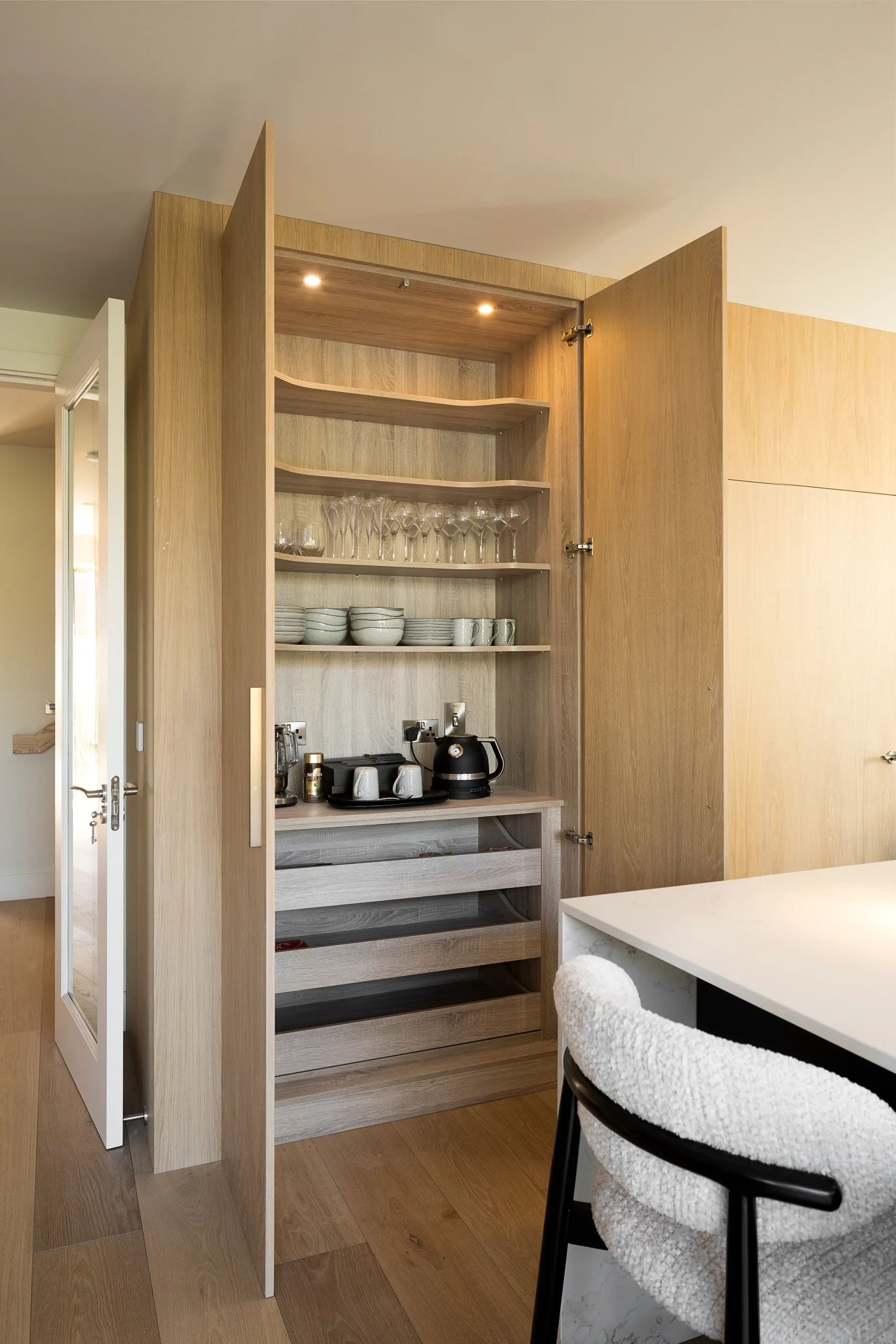 Integrated breakfast pantry with lit oak shelving, glassware, coffee station and pull-out drawers